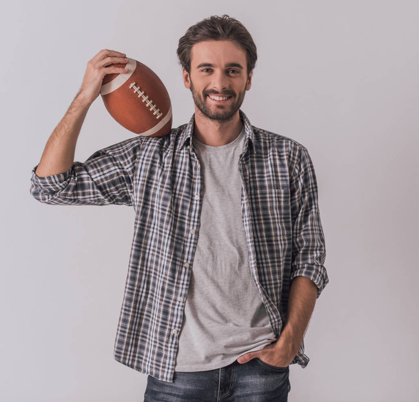 Handsome bearded man in casual clothes is holding a ball, looking at camera and smiling, on light background - Fotografie, Obrázek