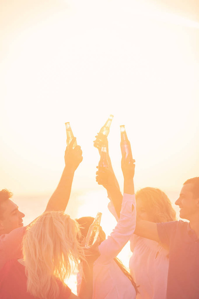 groupe de jeunes heureux avec des boissons à la plage sur le beau coucher de soleil d'été
 - Photo, image