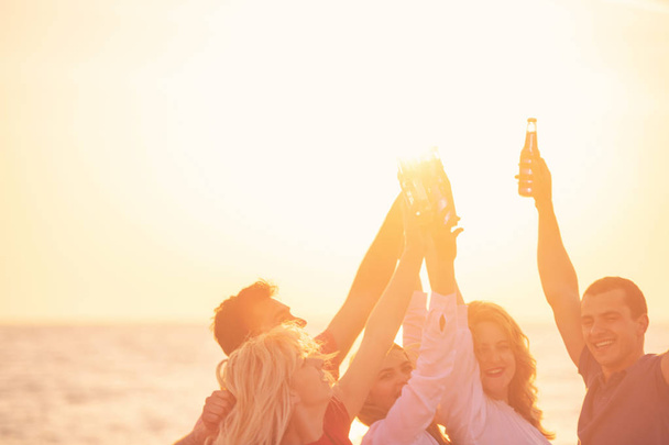 groep van gelukkige jonge mensen met drankjes op het strand op mooie zomerse zonsondergang - Foto, afbeelding