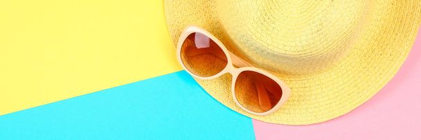 Klobouk, sluneční brýle na tříbarevné pastelové pozadí modrá, žlutá a růžová - Fotografie, Obrázek