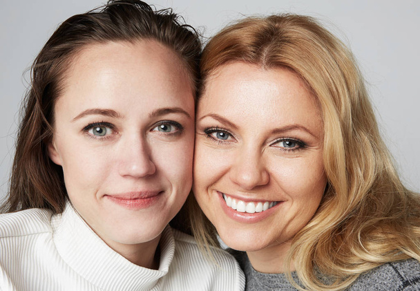zwei junge schöne Frauen mit blonden und brünetten Haaren, die auf grauem Studiohintergrund lächeln.medizinisches und kosmetisches Gesundheitskonzept für Gesichtshaut. - Foto, Bild