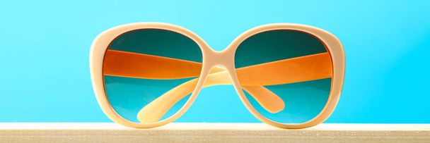 Yellow sunglasses on a wooden shelf on a blue pastel background. Minimalism - Φωτογραφία, εικόνα