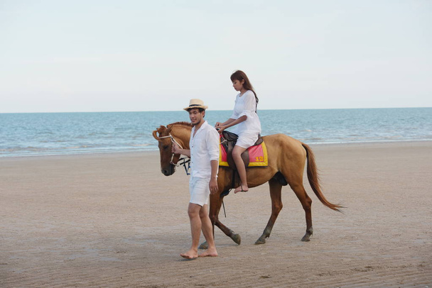 Páry a koně jdou na pláži večer před západem slunce. - Fotografie, Obrázek