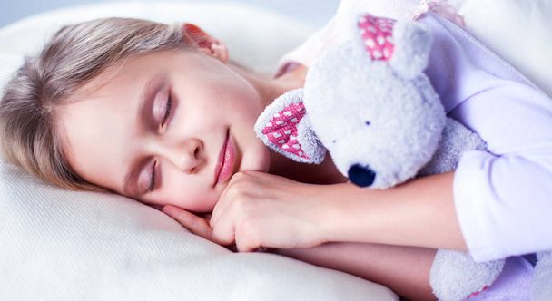 Child little girl sleeps in the bed with a toy teddy bear - Foto, Bild