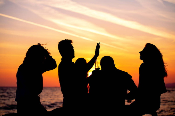 Σιλουέτες των νέων στο πάρτι στην παραλία κατά τη διάρκεια του ηλιοβασιλέματος - Φωτογραφία, εικόνα