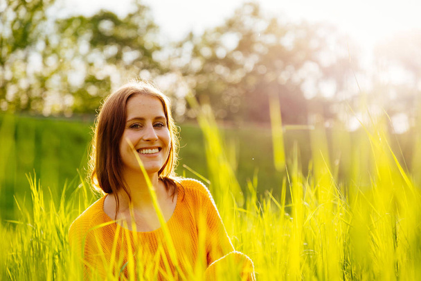 Молодая женщина, сидящая в траве на солнышке
. - Фото, изображение