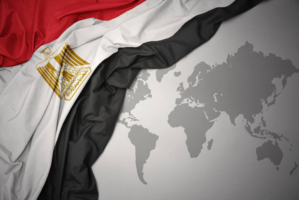 ondeando colorida bandera nacional de Egipto sobre un fondo gris mapa del mundo
. - Foto, Imagen