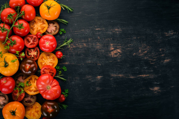 Assortment of colored fresh tomatoes. On a black wooden background. Top view. Copy space. - Photo, image