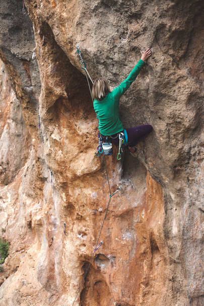 A rock climber on a rock. The girl is making an ascent. Sports in nature. Active lifestyle and fitness outdoors. An extreme hobby. Hardy woman. - Photo, Image