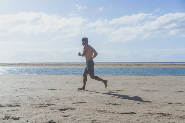 Running man jogging on beach.Muscular male runner training outside working out. - Foto, Imagen