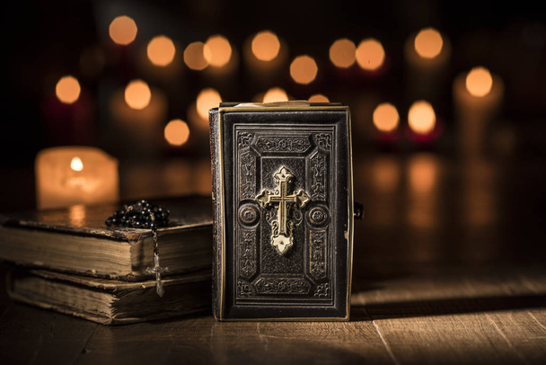 Antique precious Bible, Holy rosary and lit candles in the Church: religion and Christianity concept - Photo, Image