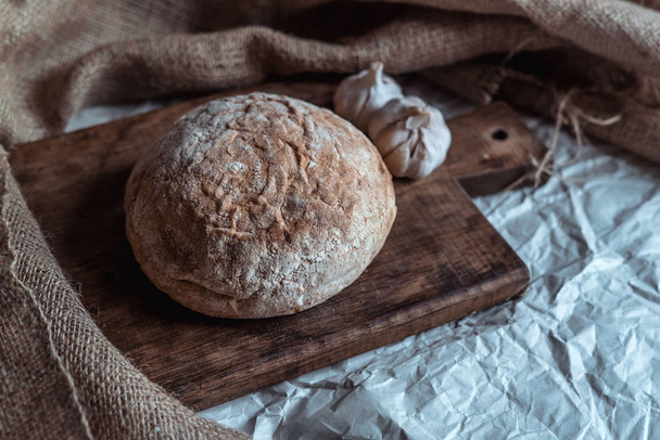 Brot mit Knoblauch und Tischdecke auf braunem Holzbrett - Foto, Bild