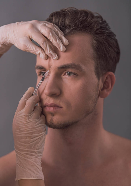 Handsome young man is getting face injection, on gray background - Φωτογραφία, εικόνα