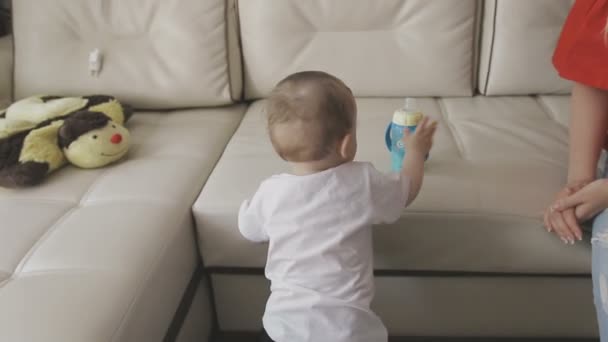 A little child drinks milk from a bottle. Family at home - Imágenes, Vídeo