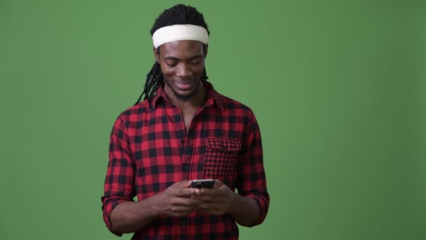 Young handsome African man with dreadlocks against green background - Materiał filmowy, wideo