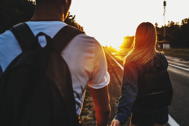 Incrível jovem casal caucasiano viajando perto da estrada olhando para o pôr do sol e segurando as mãos
. - Foto, Imagem