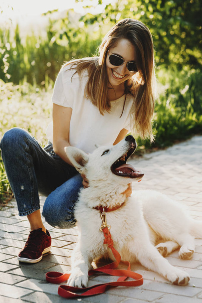 Mulher caucasiana jovem incrível em óculos de sol olhando para seu cão siberiano rindo enquanto o cão também está rindo dela na parte da manhã ao ar livre
. - Foto, Imagem
