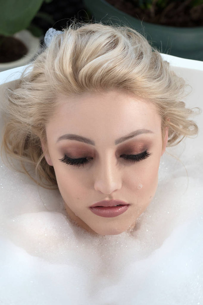 Closeup beauty portrait of one sensual attractive young woman with glamour makeup lying in bath tub with water and white soap foam . - Foto, immagini