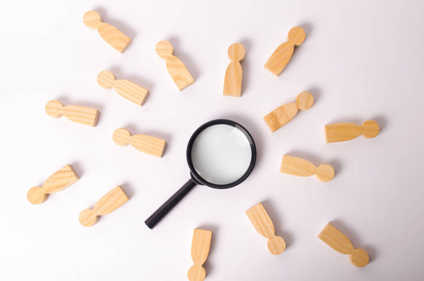Wooden figures of people lie around a magnifying glass on a white background. The concept of the search for people and workers, human resources. Hiring for work, tracing people. - Valokuva, kuva