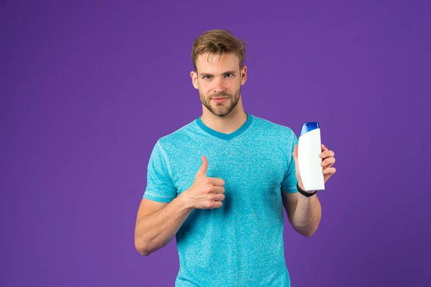 Man show thumbs up with shampoo bottle on violet background. Bearded man like gel tube on purple background. Skincare and hair care. Health and healthcare. Cosmetic for spa and bath or shower - Фото, изображение