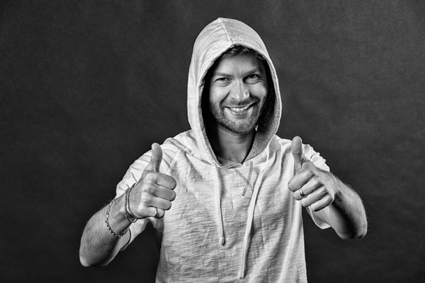 Happy man with thumbs up. Bearded man smile with beard in hood. Fashion model wear hoodie tshirt. Active lifestyle and health activity. Fashion style and trend concept, black and white - Valokuva, kuva