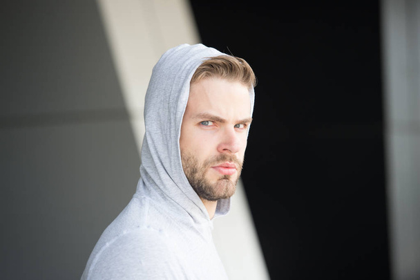 Guy bearded and attractive cares about his appearance. Man with bristle on serious face, urban background, defocused. Man with beard or unshaven guy looks handsome hooded. Skin care concept - Foto, Imagem