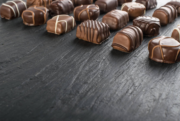 Piękne kreatywne czekoladowych słodkości na naturalne czarne tło kamienia. Mieszanka czekoladek z miejscem dla tekstu - Zdjęcie, obraz