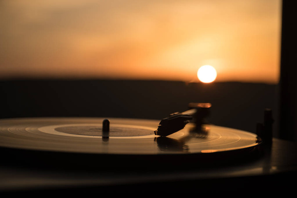 山に沈む夕日の背景にターン テーブル ビニール レコード プレーヤー。Dj ミックス ・音楽を再生するためのサウンド テクノロジー。黒のビニール レコード。ビンテージ ビニール レコード プレーヤー。ビニール レコードを針します。 - 写真・画像