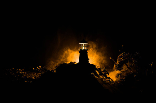 Lighthouse with light beam at night with fog. Old lighthouse standing on mountain. Table decoration. Toned background. Moonlighting. Selective focus - Photo, Image
