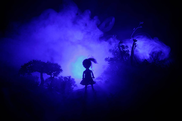 Horror Halloween decoró imagen conceptual. Una chica sola con la luz en el bosque por la noche. Silueta de niña de pie entre los árboles con luz surrealista en el fondo. Enfoque selectivo
. - Foto, Imagen