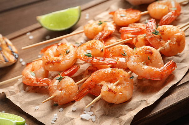 Skewers with delicious fried shrimps on wooden board, closeup - Fotó, kép
