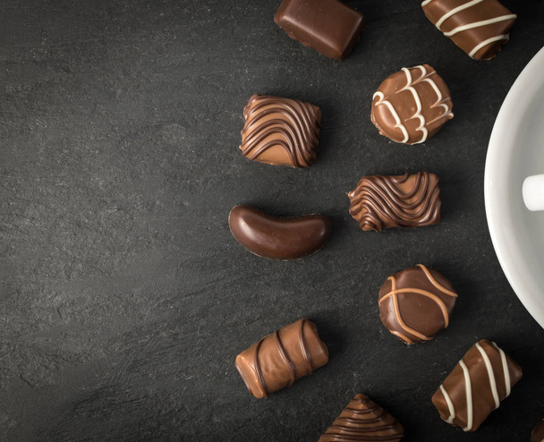 Όμορφη δημιουργική σοκολάτας γλυκά σε φυσικό μαύρο φόντο πέτρα. Μείγμα από σοκολάτες κάτοψη και επίπεδης Lay με θέση για το κείμενο - Φωτογραφία, εικόνα