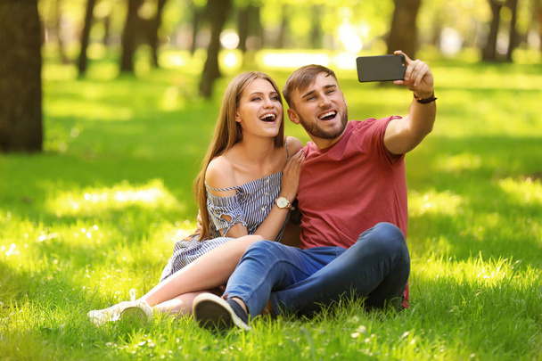 Happy young couple taking selfie on green grass in park - Photo, image