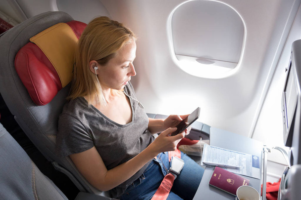 Mujer escuchando música en el teléfono inteligente en el avión de pasajeros comerciales durante el vuelo
. - Foto, Imagen