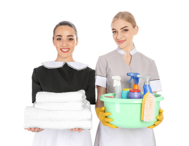 Young chambermaids with folded clean towels and detergents on white background - Φωτογραφία, εικόνα