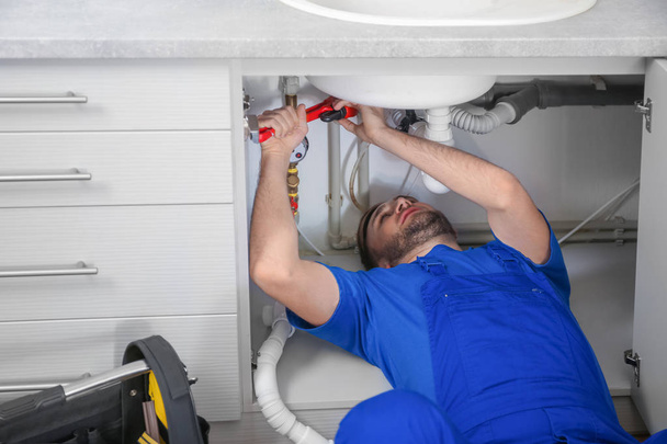 Professional plumber in uniform fixing sink with pipe wrench - Valokuva, kuva