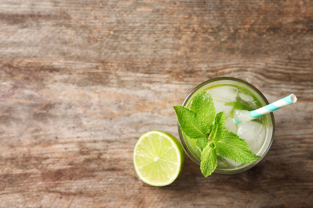 Refreshing beverage with mint and lime in glass on wooden background, top view - Fotó, kép