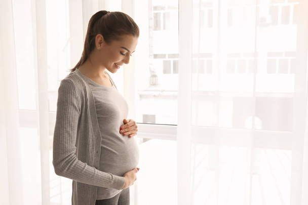 Το πρωί της όμορφη έγκυος γυναίκα να στέκεται κοντά σε παράθυρο - Φωτογραφία, εικόνα