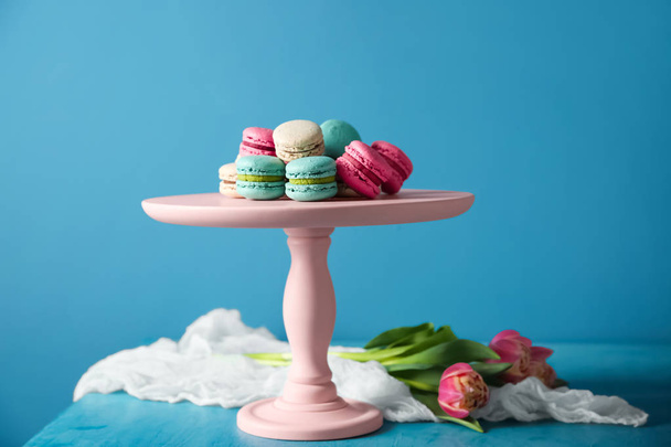 Dessertstand mit leckeren Macarons auf dem Tisch vor farbigem Hintergrund - Foto, Bild