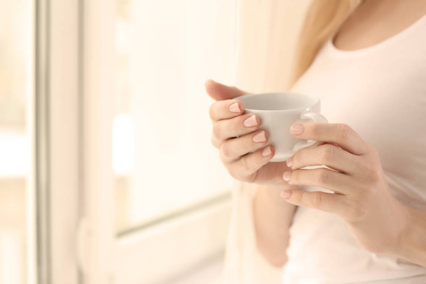 Mujer joven bebiendo café de pie cerca de la ventana en casa
 - Foto, imagen