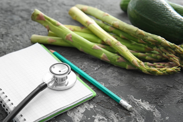 Stethoskop mit Notizbuch und gesundem Essen auf dunkelgrauem Hintergrund - Foto, Bild