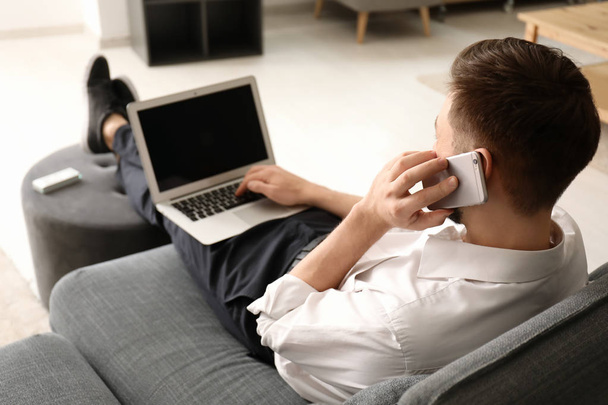 Freelancer talking on phone while using laptop at home - Photo, Image