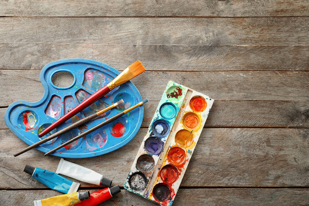 Трубки с красками, кисточками и акварелями на деревянном столе
 - Фото, изображение