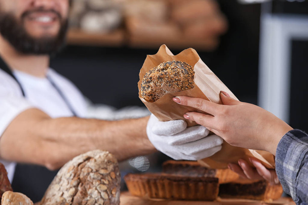 Young man giving fresh bread to woman in bakery - Photo, Image
