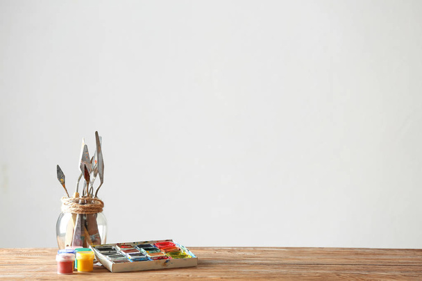 Vaso con coltelli palette e vernici su tavolo in legno su sfondo chiaro
 - Foto, immagini