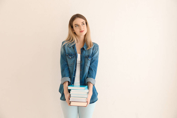 Νεαρή γυναίκα με βιβλία κοντά φωτός τοίχο - Φωτογραφία, εικόνα