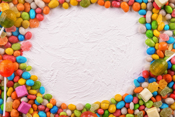 Marco hecho de caramelos de colores sobre fondo blanco texturizado
 - Foto, Imagen