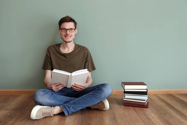 Genç adam renk duvarının yakınında katta otururken kitap okuma - Fotoğraf, Görsel