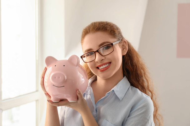 Young woman holding piggy bank indoors. Money savings concept - Foto, Bild