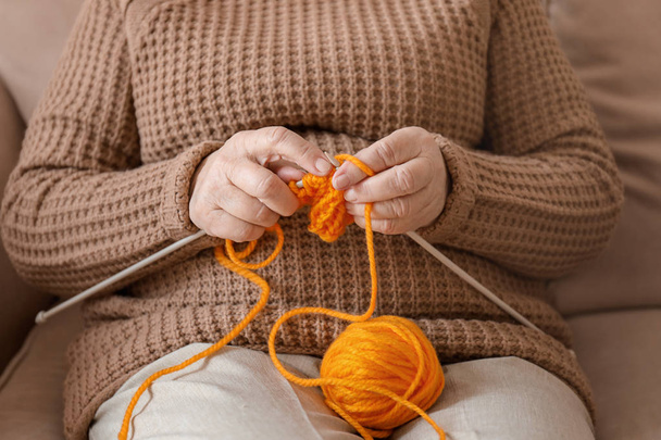 Femme âgée assise sur le canapé tout en tricotant pull à la maison
 - Photo, image